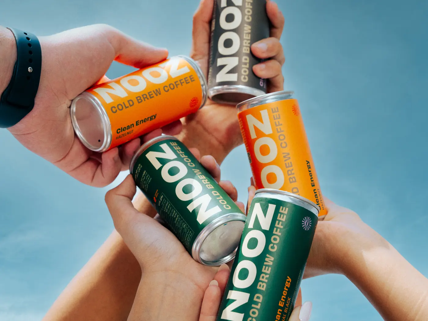 Four hands raising NOOZ cans in a toast