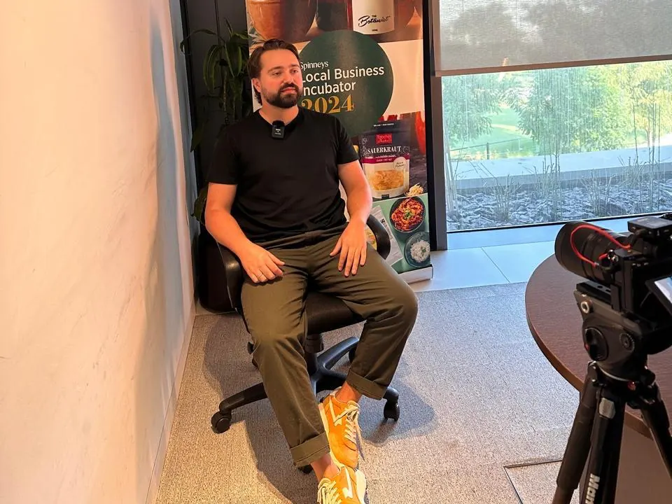 Timur El Ait seated for a filmed interview in front of the Spinneys Local Business Incubator 2024 banner
